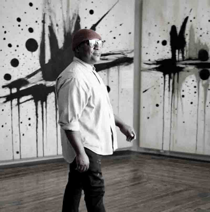 Porträt von Sommelier André Hueston Mack in einem hellen Hemd und roter Strickmütze vor abstrakter schwarz-weißer Kunst.