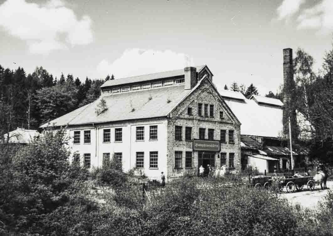 Schwarz-weiß-Aufnahme eines alten, mehrstöckigen Industriegebäudes aus Ziegelstein mit einem großen Satteldach. Über dem Eingang ist ein Schild mit der Aufschrift 'Josephinenhütte' zu sehen.