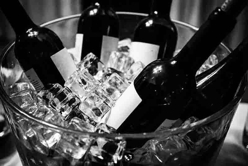 Eine kontrastreiche Schwarz-Weiß-Fotografie die mehrere Weinflaschen in einem gläsernen Eiskübel zeigt. Die Flaschen ragen diagonal aus einer Masse von klar definierten, quadratischen Eiswürfeln heraus.