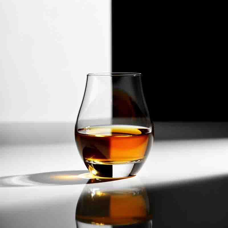 Eine minimalistische Studioaufnahme eines bauchigen Whisky-Nosing-Glases, das zur Hälfte mit bernsteinfarbener Flüssigkeit gefüllt ist.